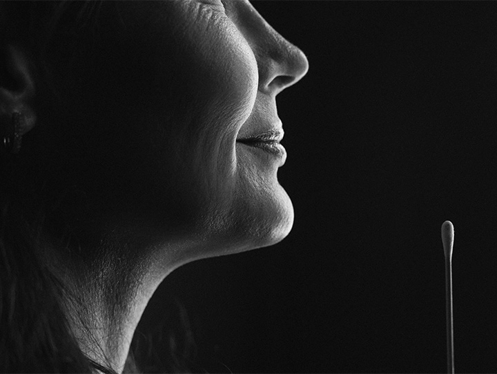 Grayscale close-up profile of a woman’s face and neck, highlighting skin texture, wrinkles, and facial features. Her expression is neutral. A small cotton swab extends upward from the lower right into a black background. Dramatic lighting emphasizes contrast and detail, giving the image a portrait or medical illustration quality. - Necklift in Carmel, IN